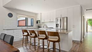 Una cocina moderna con armarios blancos, un refrigerador de acero inoxidable y una isla central con taburetes de bar.