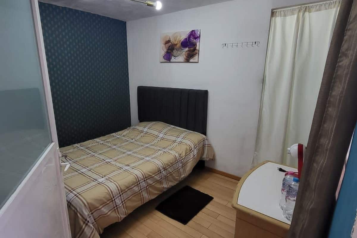 Un dormitorio pequeño con cama, un escritorio, una botella de agua y una lámpara en el techo.