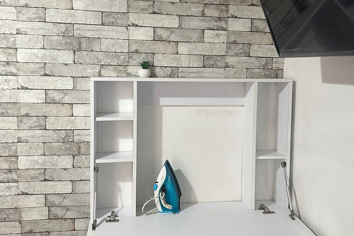 Una habitación con pared de ladrillo, un escritorio blanco con estanterías y una pequeña planta en maceta en la pared.