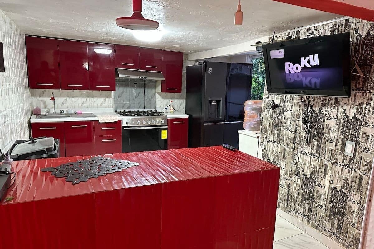 Una cocina con gabinetes rojos, un refrigerador negro y un televisor mostrando 'RoKu Bokn'.