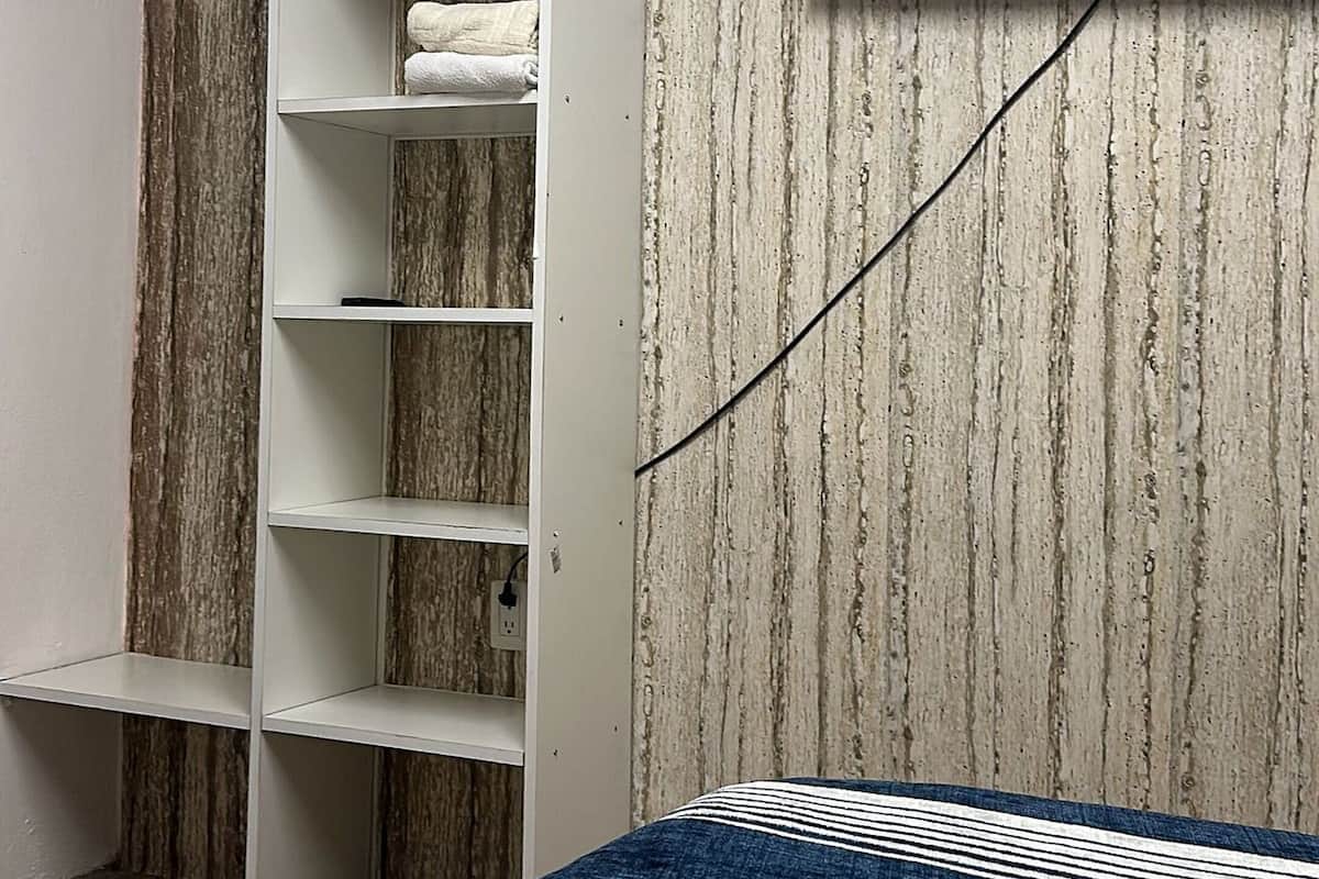 Un dormitorio con una cama, un armario blanco, un televisor montado y una pared de madera.