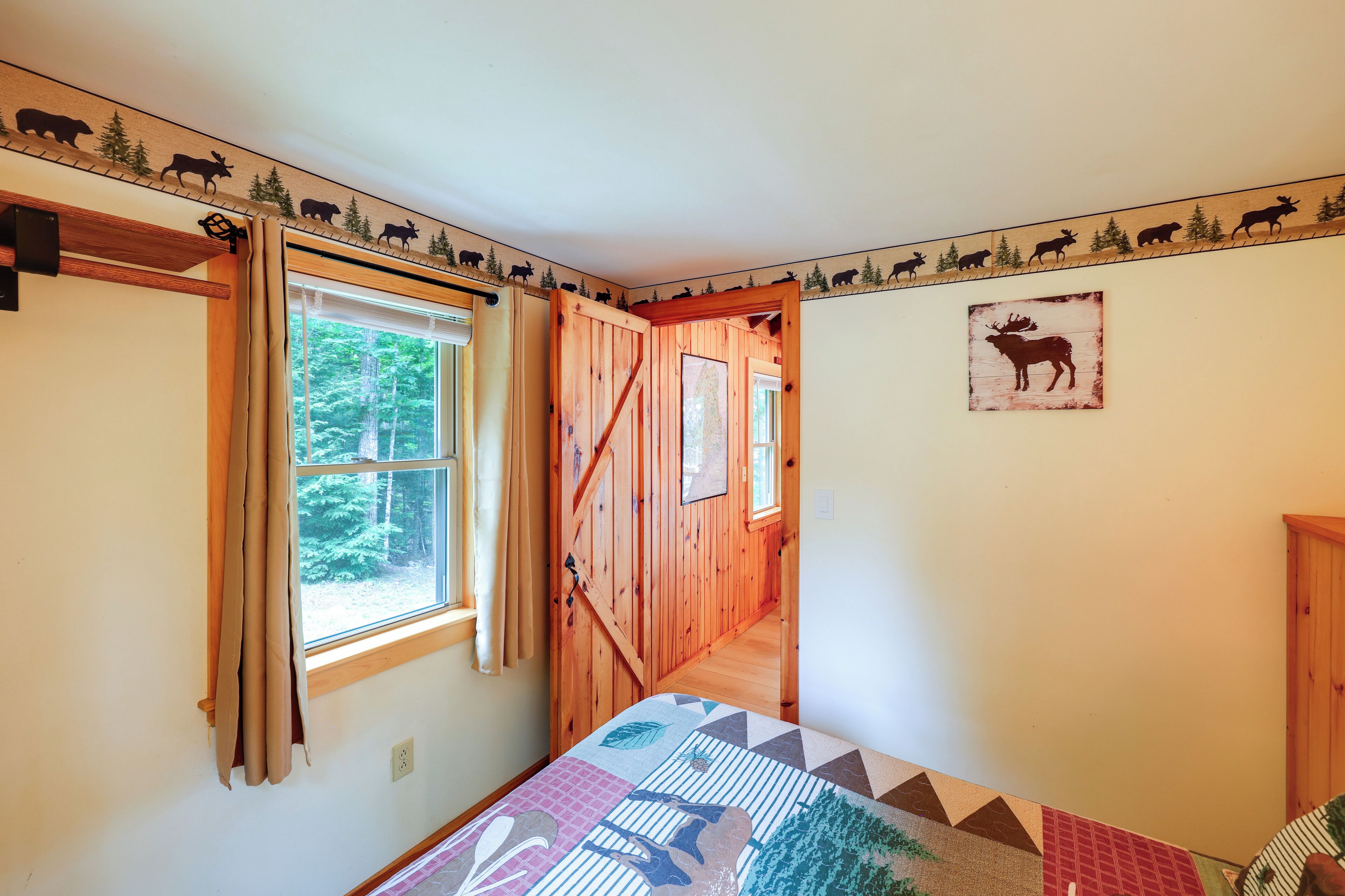 A bedroom with a bed, a window with curtains, a wooden door, and a wall with animal silhouettes.