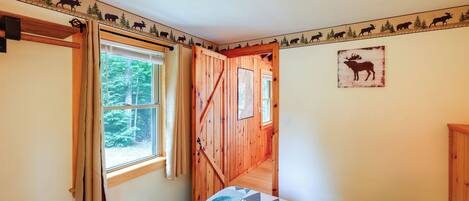 A bedroom with a bed, a window with curtains, a wooden door, and a wall with animal silhouettes.