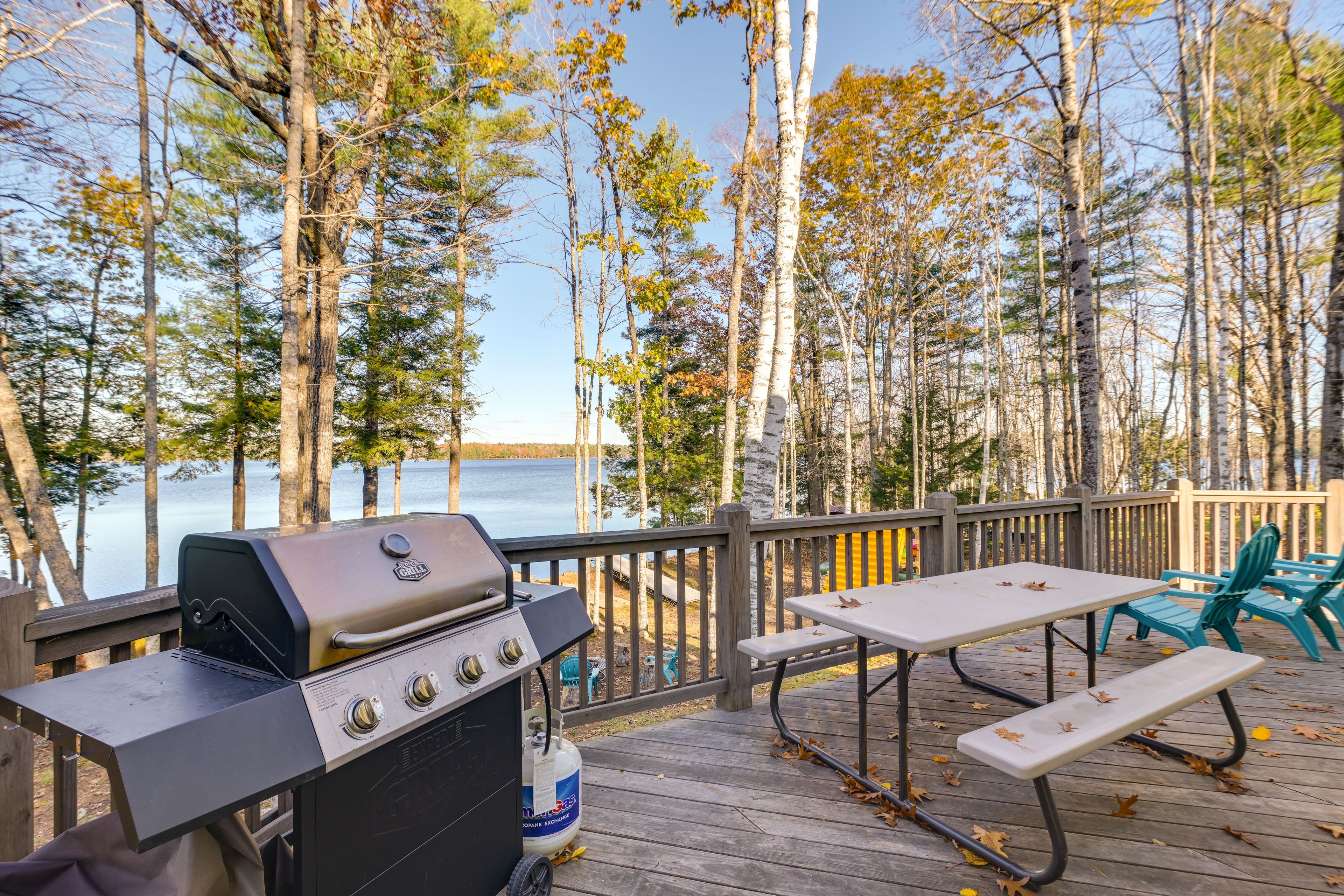 Une terrasse avec un barbecue, une table de pique-nique et des chaises, donnant sur un lac.