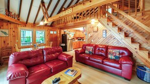 A log cabin interior with a red leather sofa, wooden staircase, and a kitchen area.