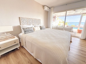 Ein Schlafzimmer mit einem großen Bett, einem Nachttisch, einem dekorativen Kopfteil und Blick aufs Meer.