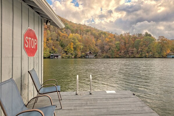 A wooden dock with metal chairs, a stop sign, and a view of a lake with autumn foliage in the background.