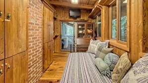 A wooden cabin interior with a bed, a television, and a brick wall. - T Landing Top & Bottom Units (Clayton)