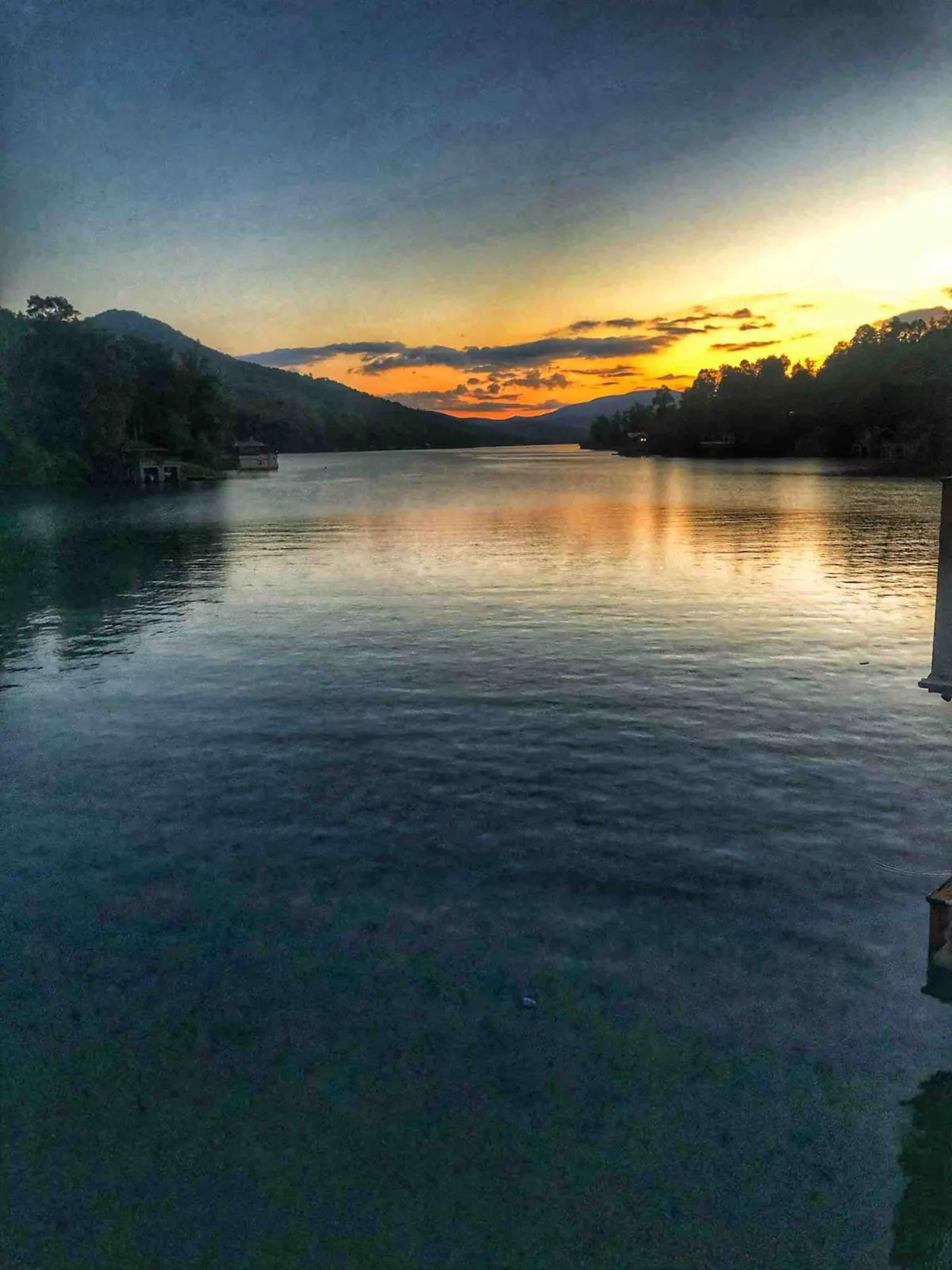 Un lago tranquilo al atardecer, con un pequeño muelle a la izquierda y un edificio a la derecha.