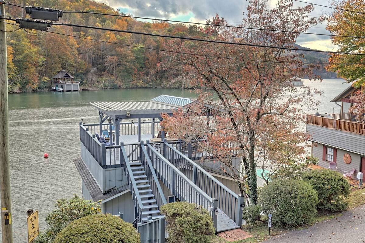 A lakeside cabin with a dock, a staircase leading to a deck, and a small building with a red roof.