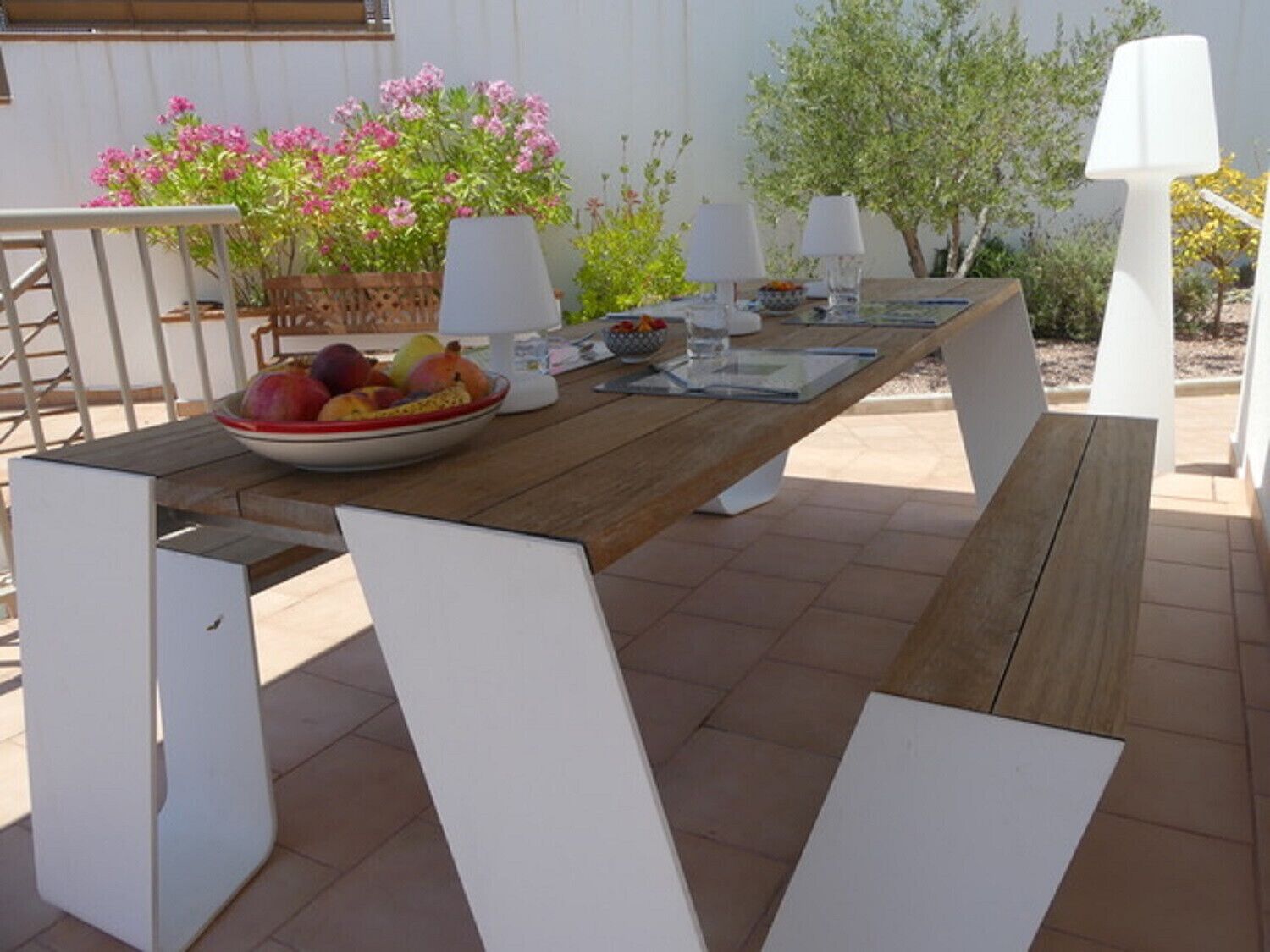 An outdoor dining area with a wooden table, white chairs, and a bowl of fruit.