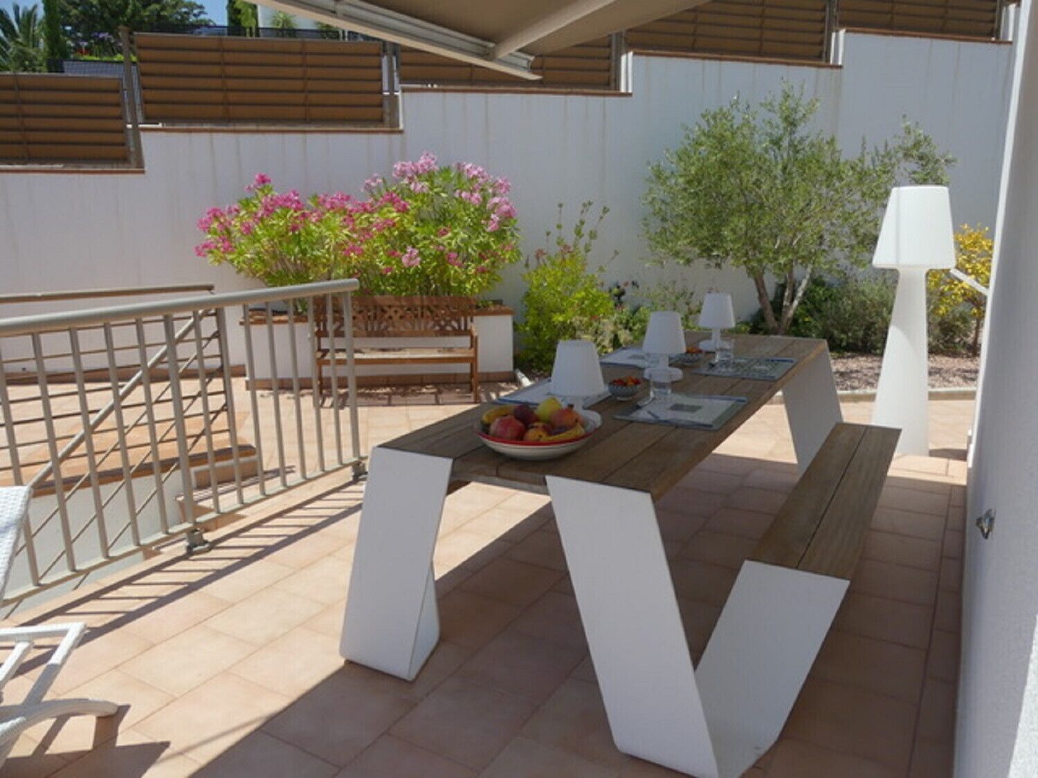An outdoor patio with a wooden table set for dining, surrounded by white chairs.