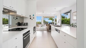 A modern kitchen with white cabinetry, a black stovetop, and a view to a balcony with outdoor furniture. - Chic Beachside Abode, Sunrise Beach (Sunrise Beach)