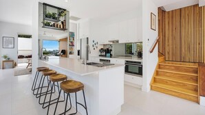 A modern kitchen with a central island, bar stools, and a view of the outdoors. - Chic Beachside Abode, Sunrise Beach (Sunrise Beach)