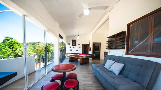 Ein geräumiger Balkon mit Billardtisch, grauem Sofa und roten Barhocker.