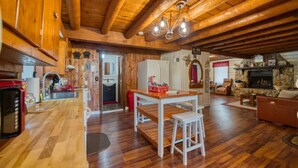 Un accogliente interno di una baita con pavimento in legno, zona pranzo, camino e cucina.
