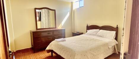 Quarto com cama, cômoda e uma pequena janela.