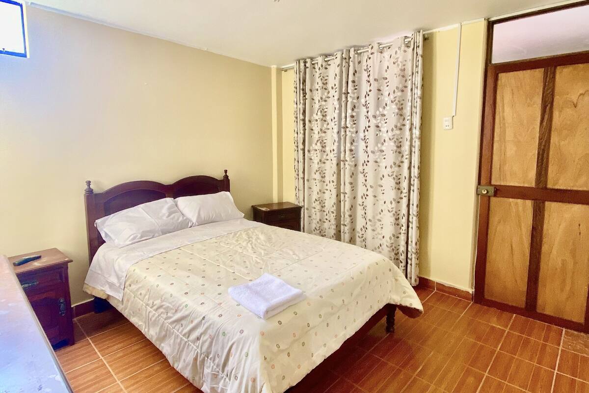 A bedroom with a bed, a nightstand, a wooden door, and a window.