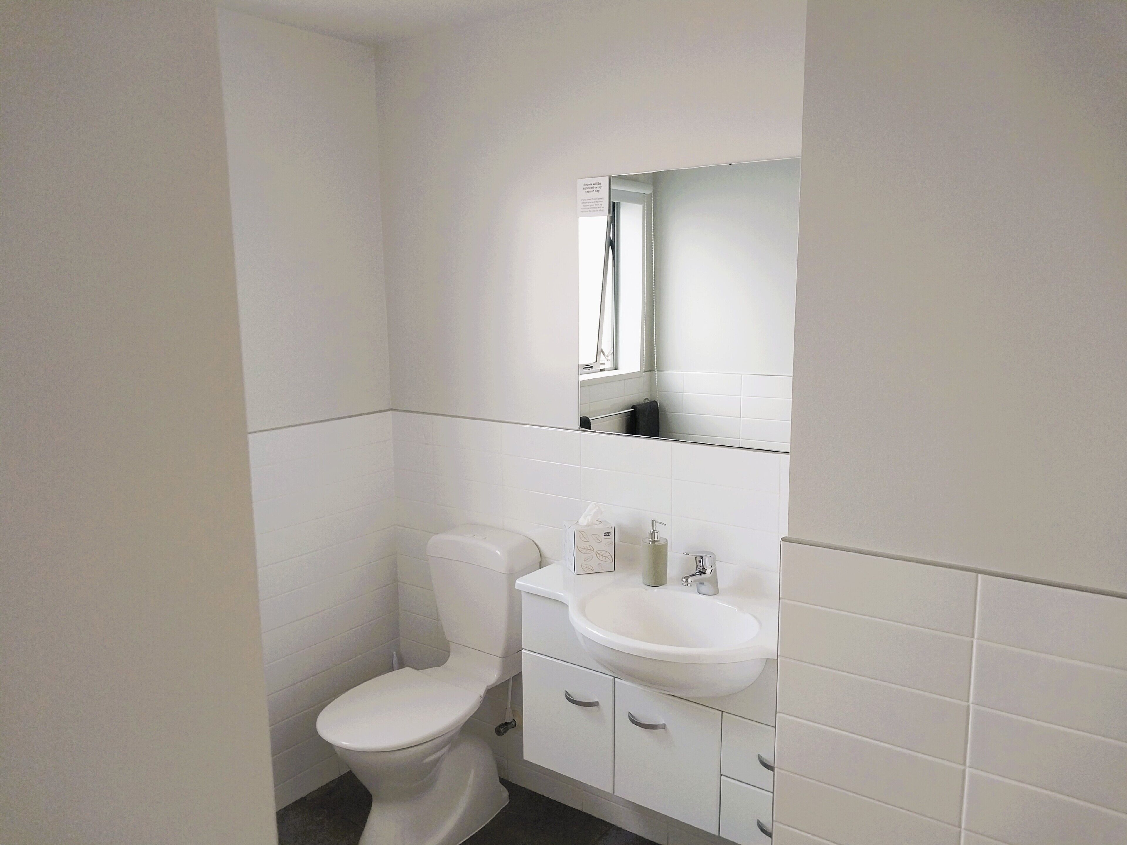 Un baño pequeño y blanco con inodoro, lavabo y espejo sobre él.
