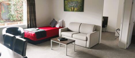 A furnished living room with a bed, sofa, coffee table, and a painting on the wall.