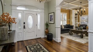 Un salón amplio con suelo de madera, una grande mesa de centro oscura, un sofá negro y una araña.