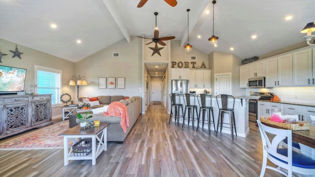 A spacious living area with a sofa, coffee table, and TV, a kitchen with bar stools, and a ceiling fan. - Private Pool Retreat Walk to Beach 2 Living Spaces + Game Room for Groups (Port Aransas)