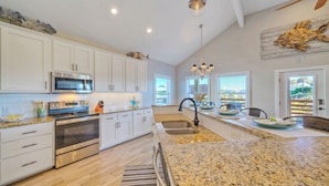 A modern kitchen with white cabinets, stainless steel appliances, granite countertops, and a large island with a sink. - Private Pool Retreat Walk to Beach 2 Living Spaces + Game Room for Groups (Port Aransas)