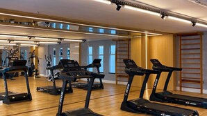 A gym with treadmills, exercise equipment, and a wooden floor.