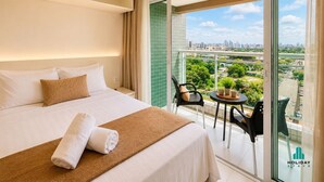 A hotel room with a bed, a small table with chairs, and a balcony with a city view.