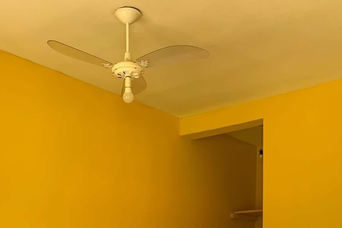 Un dormitorio con cama, almohadas, un ventilador de techo y una puerta que da a otra habitación.
