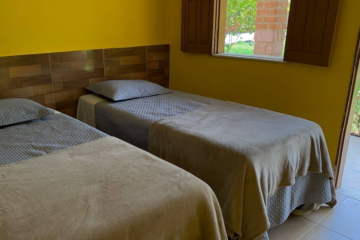 Una habitación con dos camas individuales, cabecera de madera, ventana con cortinas y pared amarilla.