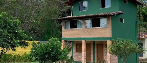 A two-story house with a green exterior, a brick base, and a small garden area in front.