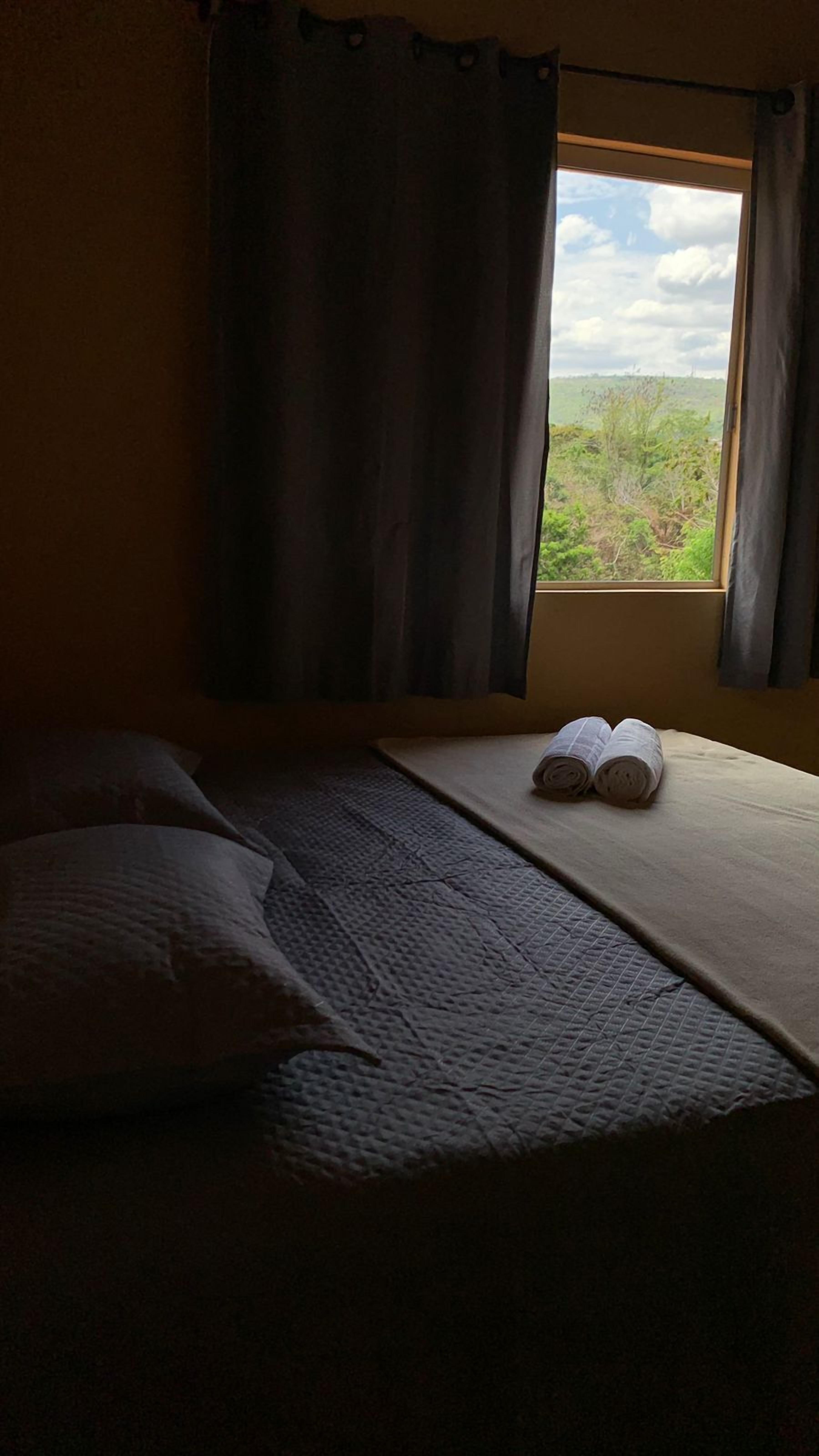 A room with a bed, a window with curtains, and a view of greenery outside.
