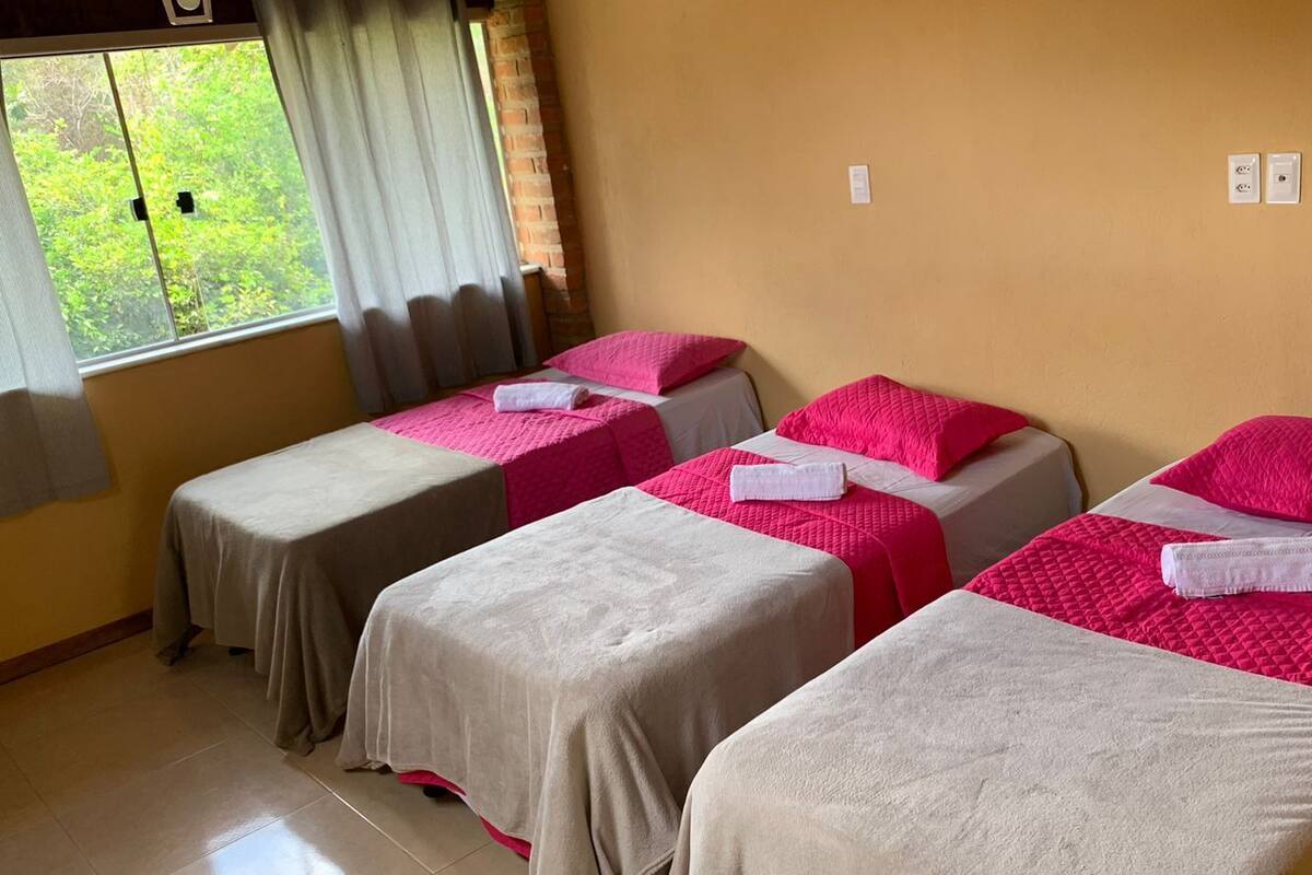 Una habitación con cuatro camas, cada una con una colcha rosa y beige, y una ventana con cortinas.