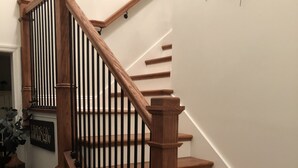 Eine Holztreppe mit schwarzer Geländer, weißen Wänden und einem kleinen Schild links.