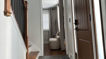 Un pasillo con una escalera de madera, un tapete estampado, una puerta con ventanal y un globo terráqueo en la pared.