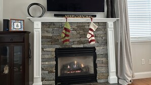 Ein Kamin mit zwei Weihnachtssocken, darüber ein Flachbildfernseher und ein Schild mit der Aufschrift 'Merry Christmas'.