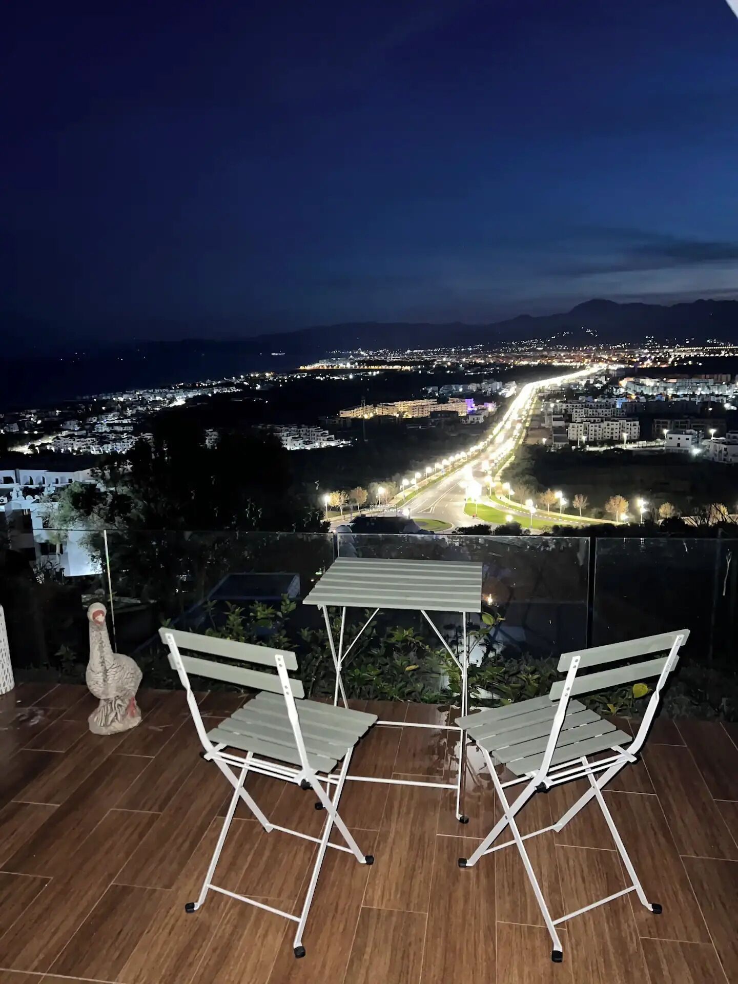 Eine Terrasse mit Tisch und Stühlen mit Blick auf eine nächtliche Stadtlandschaft.