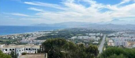 A coastal view with a clear sky, a grassy area, and a distant cityscape.