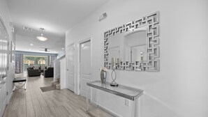 A modern hallway with a glass console table, a decorative mirror, and a staircase leading to a living area. - ⭐⭐⭐⭐⭐Spacious 10-BR Family Retreat Near Disney, Solterra Resort - Pool Spa, Game (Davenport)