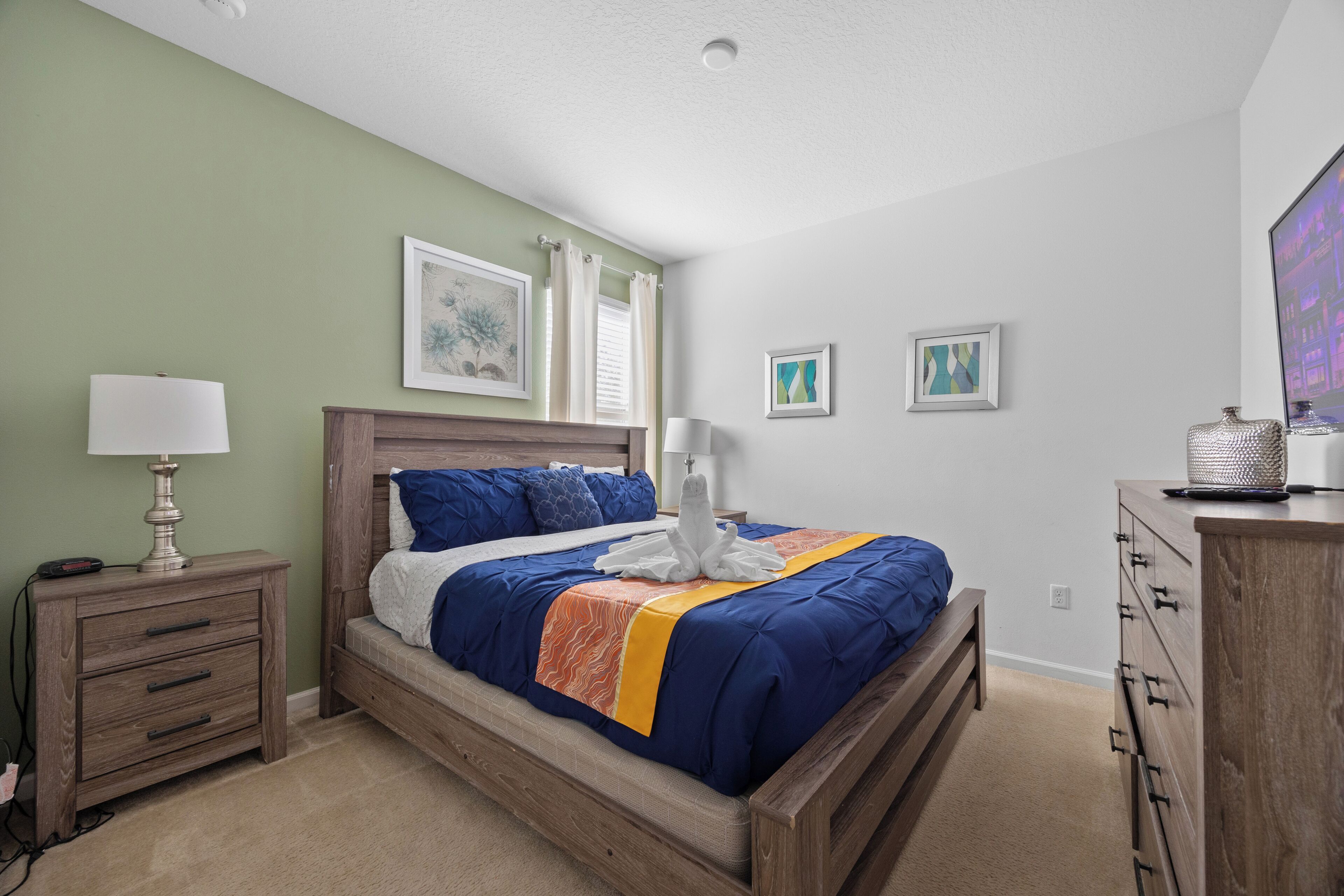 A neatly arranged bedroom with a wooden bed, a nightstand, a dresser, and a wall-mounted TV.