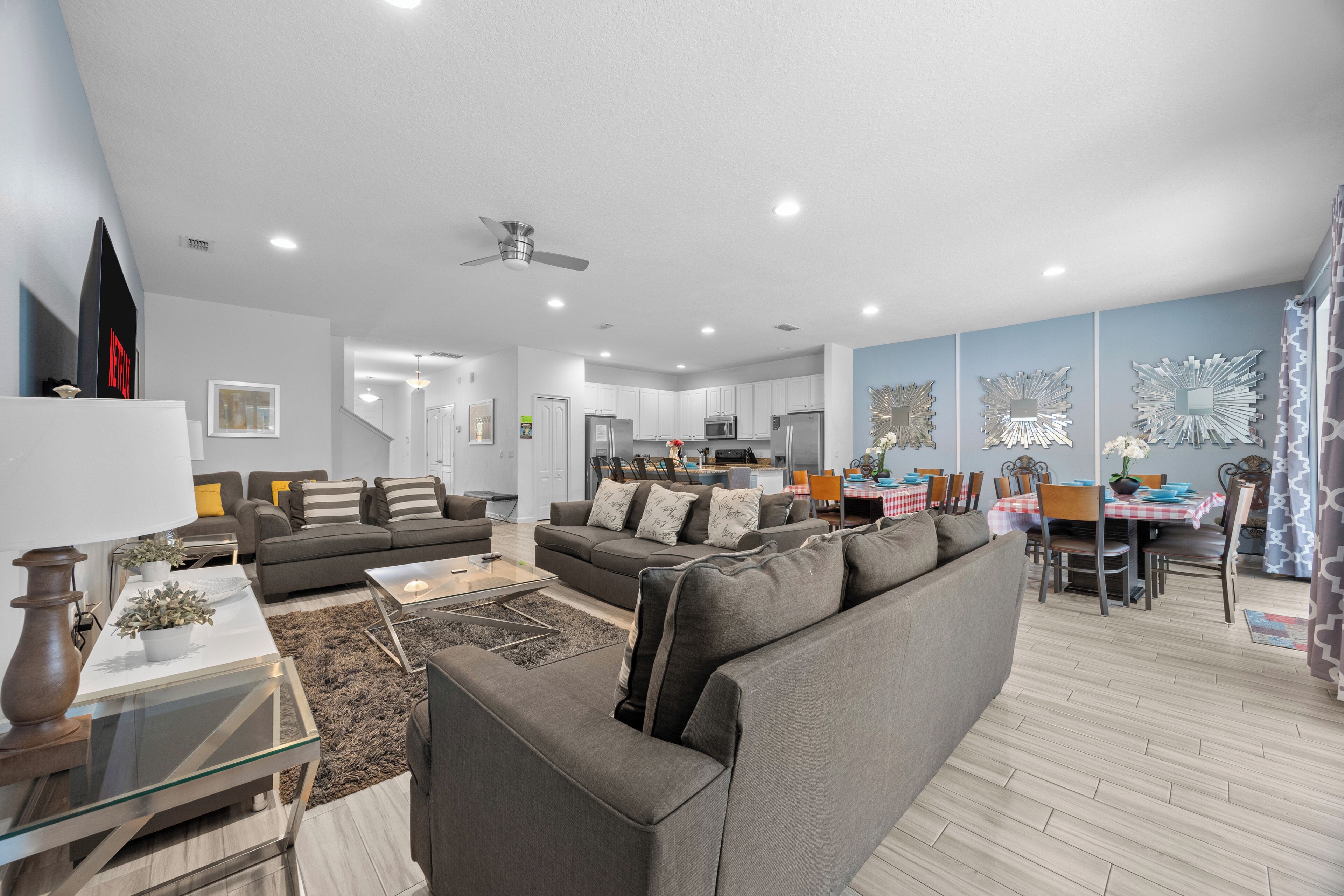 A modern living room with a grey sofa, a glass coffee table, and a dining area with a checkered tablecloth.