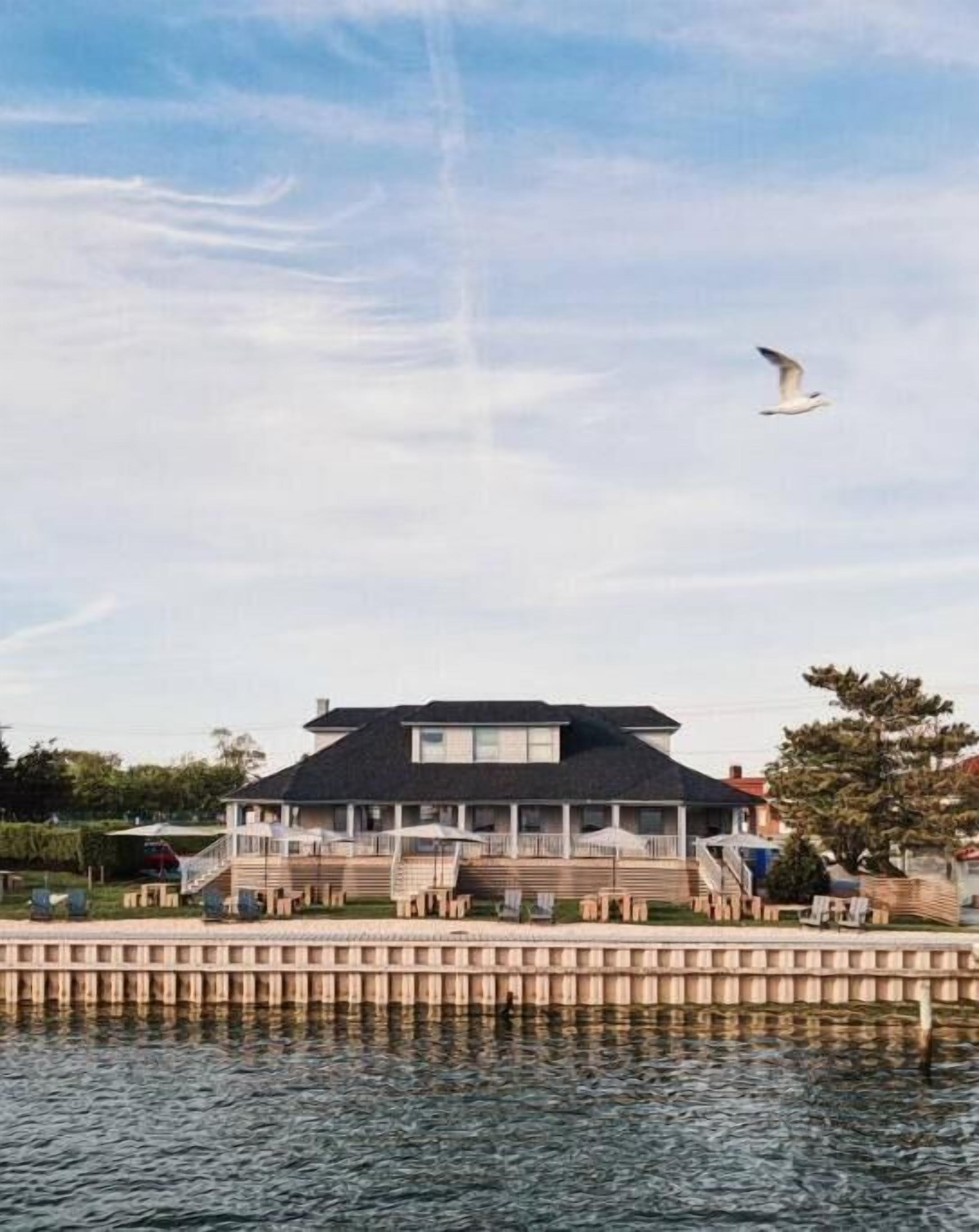 A waterfront property with a large house featuring a balcony and a staircase leading to the entrance.