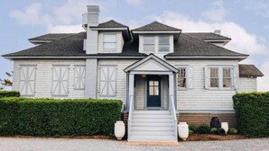 Une maison à deux étages, dotée d’une façade symétrique, d’une entrée centrale avec un petit porche et d’une cheminée.
