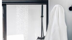 Une salle de bain moderne avec une douche à parois de verre, une serviette blanche accrochée au mur et une pomme de douche noire.