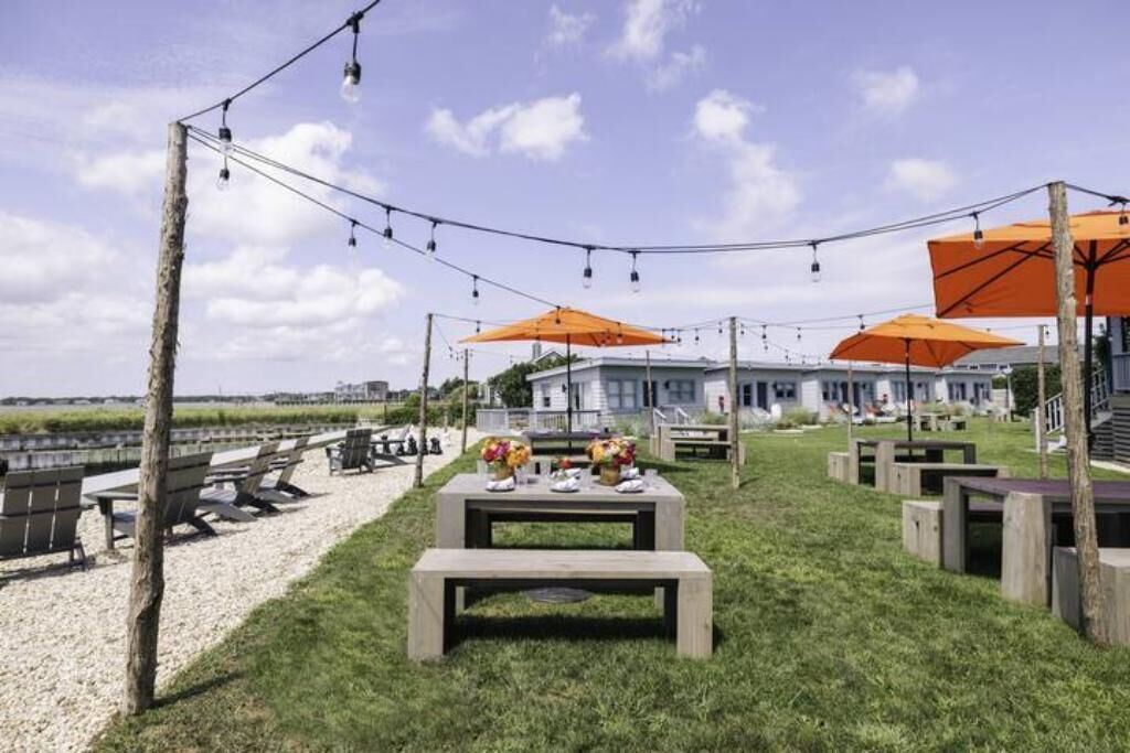 An outdoor seating area with tables and benches, string lights, and orange umbrellas.