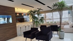 A modern reception area with a counter, black chairs, and large windows. - Living (Poços de Caldas)