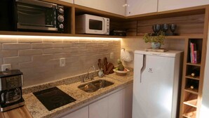 A modern kitchen with white cabinets, a built-in microwave, a stainless steel sink, and a white refrigerator. - Living (Poços de Caldas)