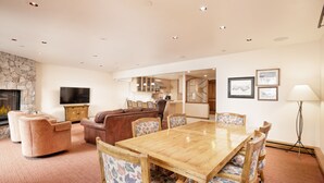 A spacious living area with a fireplace, a wooden dining table with floral chairs, a leather sofa, and a television. - North Of Nell, Unit 4b (Aspen)