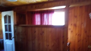 A room with wooden walls, a window with pink curtains, and a door with a glass panel. - Hostal Gomero (Santa Cruz)